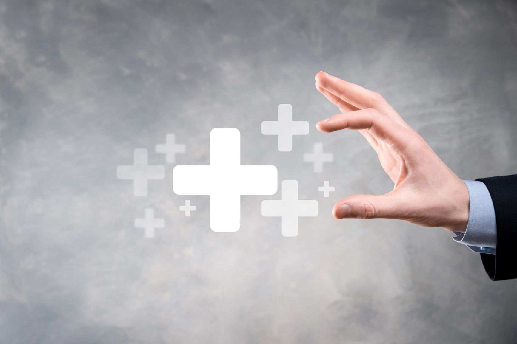 szare tlo, znaki graficzne plus, dloń, która chce ich dotknąć